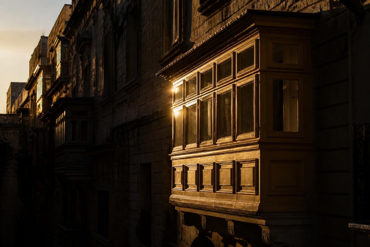 A Maltese gallarija balcony catching low golden light on a Valletta street